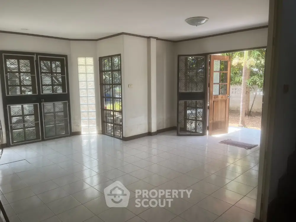 Spacious and sunlit living room with gleaming tiled floors, large windows, and glass doors leading to an inviting outdoor area, perfect for entertaining or relaxing.
