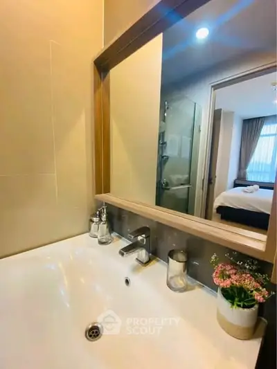 Modern bathroom with sleek sink and mirror, view into cozy bedroom with natural light.