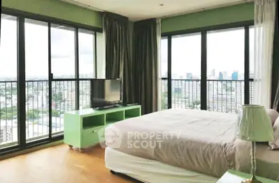 Spacious bedroom with panoramic city views and modern decor in high-rise apartment.