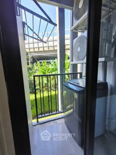 Compact balcony with washing machine and lush green view, perfect for urban living convenience.