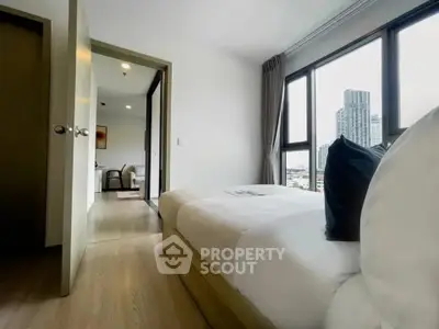 Modern bedroom with city view and natural light, featuring sleek wooden flooring and cozy bedding.