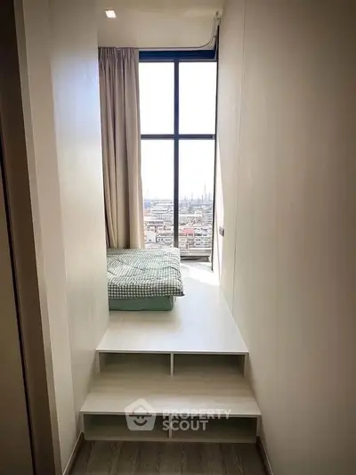 Compact bedroom with elevated bed and panoramic city view through large window.