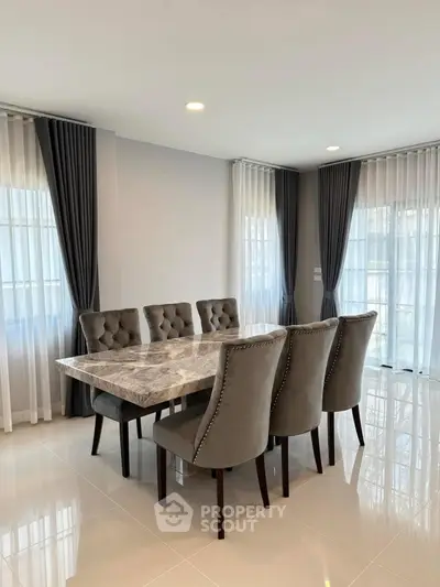 Elegant dining room with marble table and plush chairs, featuring large windows and modern curtains.