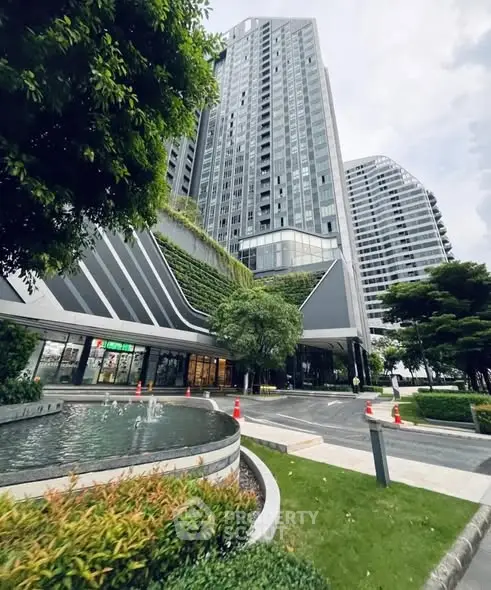 Modern high-rise building with lush greenery and water feature in urban setting.