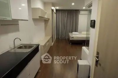 Modern studio apartment with sleek kitchen and cozy bedroom area, featuring wood flooring and neutral decor.