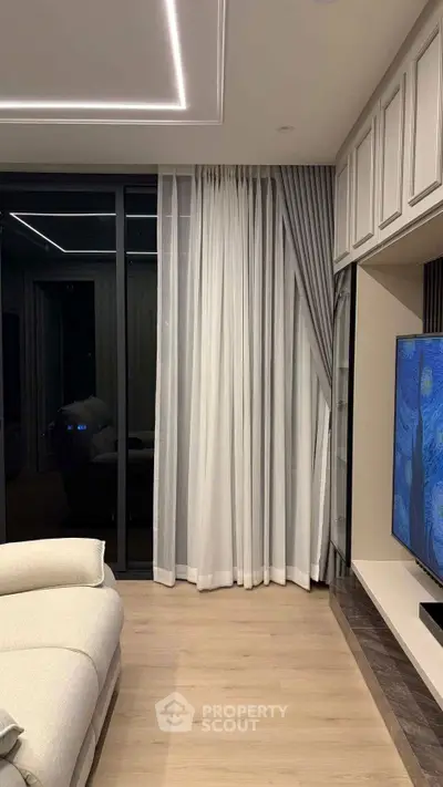 Modern living room with sleek design, featuring a large TV and elegant curtains.