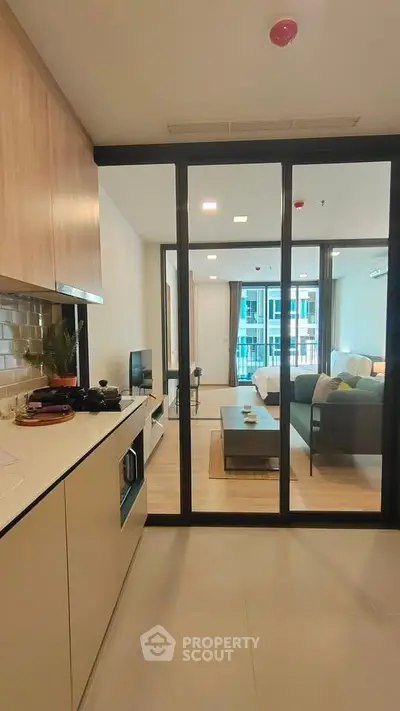 Modern open-layout kitchen leading to a stylish living room with large windows and natural light.