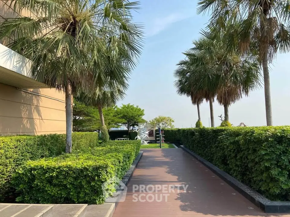 Lush garden pathway with palm trees and manicured hedges leading to a serene outdoor space.