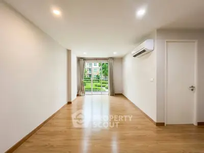 Spacious empty living room with wooden flooring and large window view.