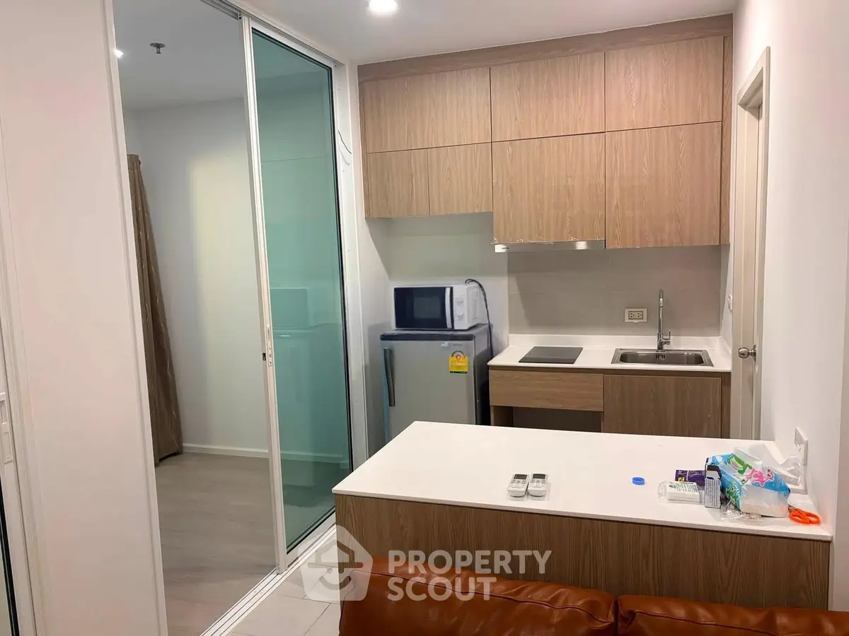 Modern compact kitchen with wooden cabinets and sleek appliances in a cozy apartment setting.