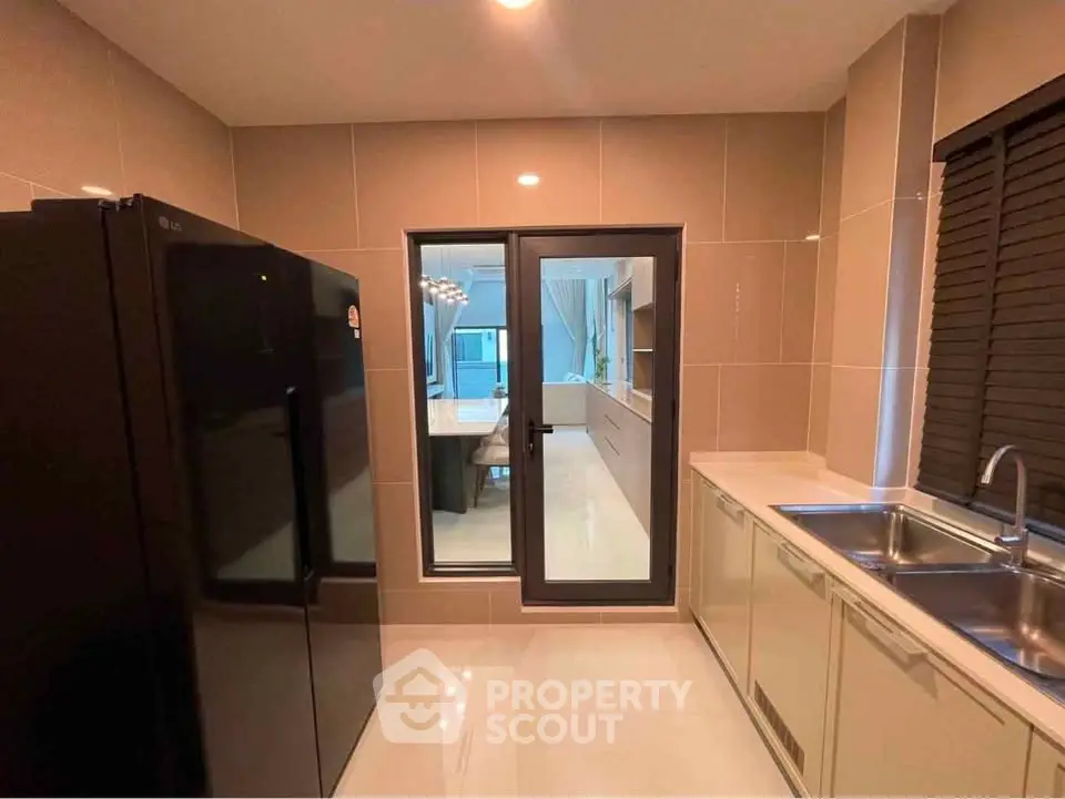 Modern kitchen with sleek black fridge and dual sink, featuring a view into the dining area.