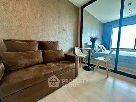 Modern living room with brown sofa and glass partition to bedroom, featuring stylish decor.