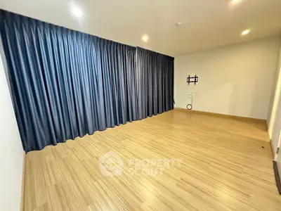 Spacious empty room with wooden flooring and dark curtains, ideal for customization.