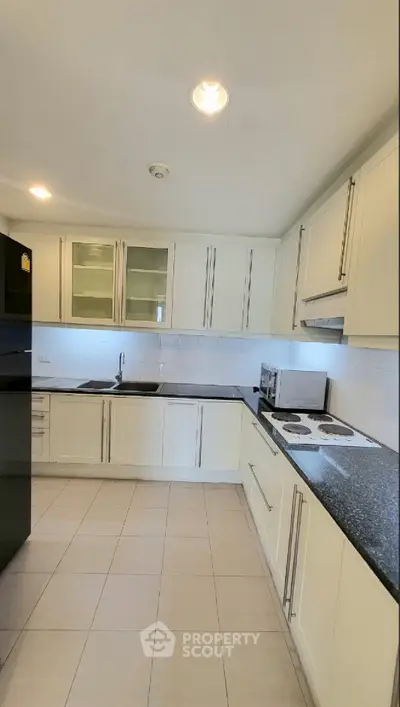 Modern kitchen with sleek black countertops and white cabinetry, featuring a closed layout and built-in appliances.