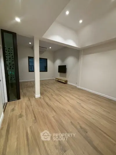 Spacious modern living room with wooden flooring and mounted TV, perfect for cozy gatherings.