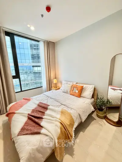 Bright and cozy bedroom with large window and modern decor in a high-rise apartment.