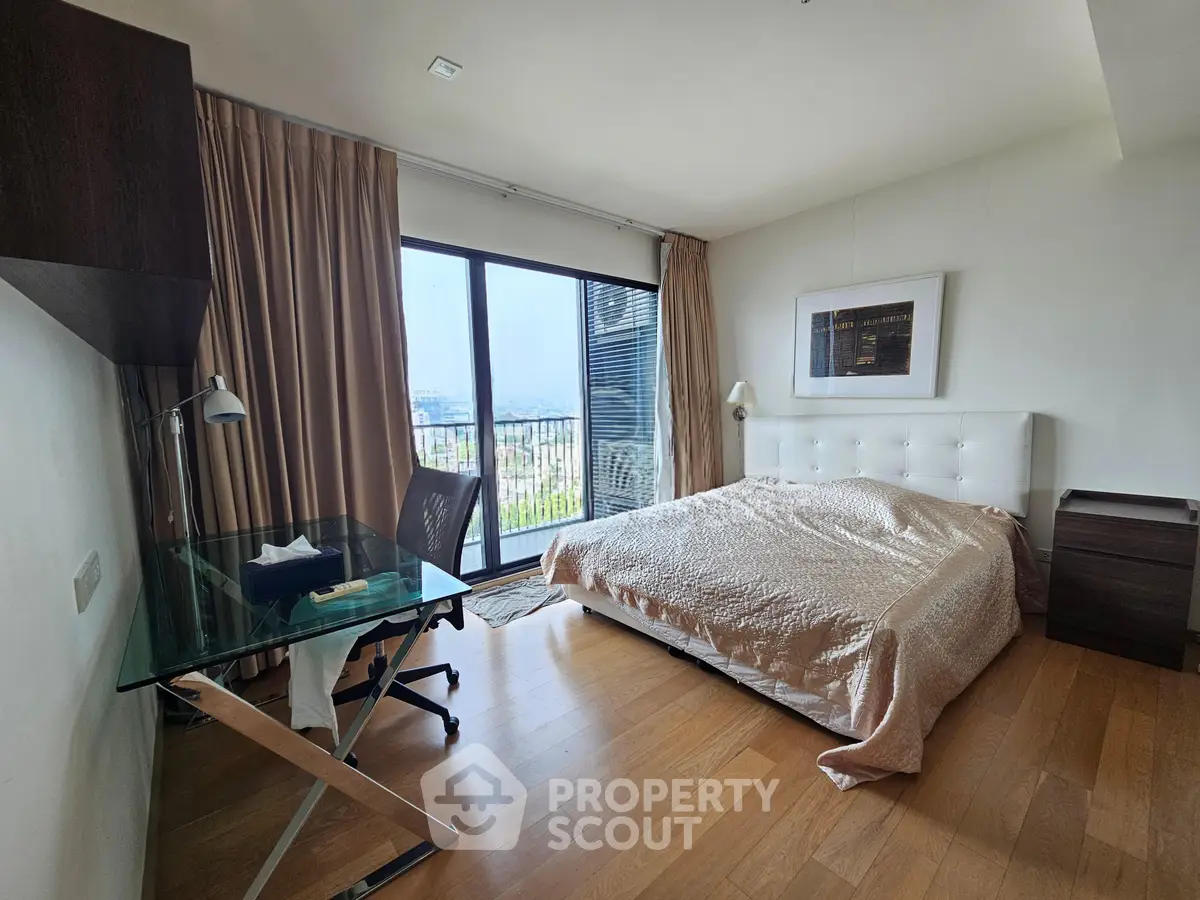 Spacious bedroom with large window and city view, featuring modern furniture and wooden flooring.