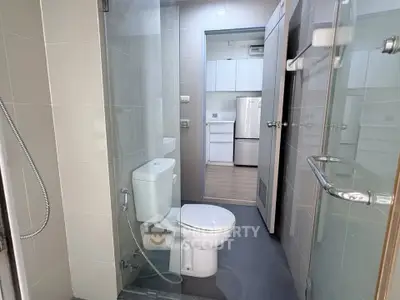 Modern bathroom with glass shower and view into sleek kitchen area.