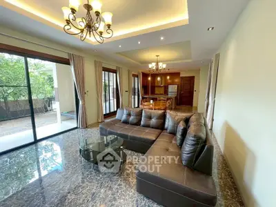 Spacious living room with elegant leather sofa and modern lighting, opening to a lush garden view.
