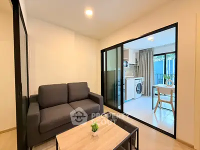 Modern living room with cozy sofa and open kitchen featuring washing machine and dining area.