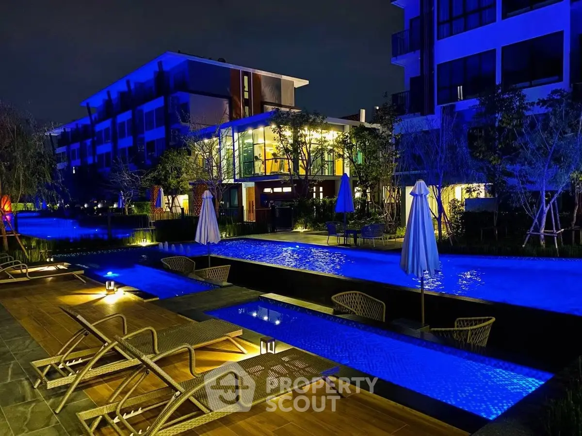 Luxurious night view of a modern apartment complex with illuminated pool and stylish outdoor seating.