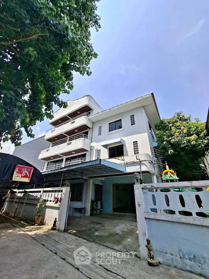 Charming multi-story residential building with spacious driveway and lush greenery, perfect for urban living.