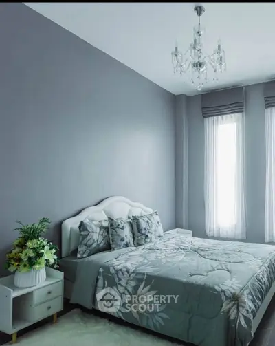 Elegant bedroom with floral bedding and chandelier, featuring natural light from tall windows.
