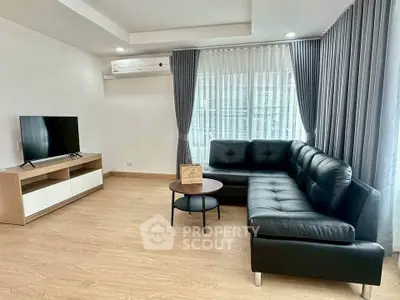 Modern living room with sleek black leather sofa and flat-screen TV, featuring elegant curtains and wooden flooring.