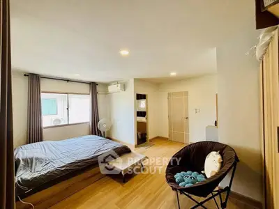 Spacious bedroom with modern decor and natural light, featuring a cozy seating area and wooden flooring.