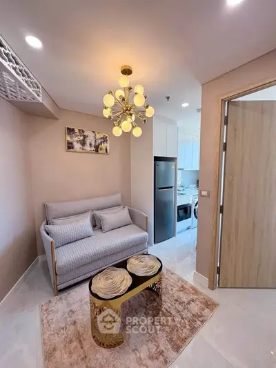 Stylish living room with modern chandelier and cozy sofa, open view to sleek kitchen with stainless steel appliances.