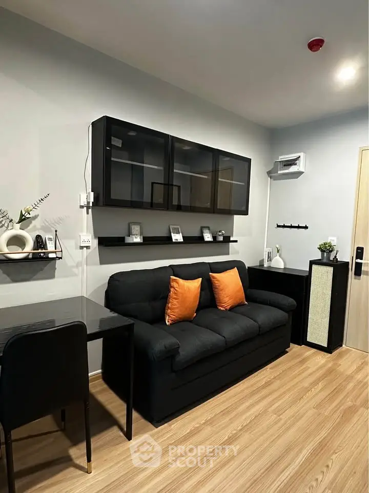 Modern living room with sleek black sofa, wooden flooring, and stylish wall-mounted shelves.