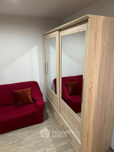 Cozy bedroom with mirrored wardrobe and red sofa, perfect for stylish living.