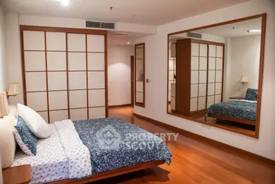 Spacious bedroom with wooden flooring and large mirror, featuring a cozy bed and elegant decor.