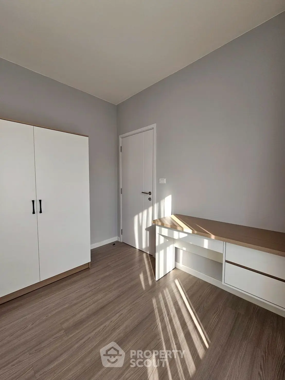 Modern minimalist room with sleek wardrobe and desk, featuring stylish wood flooring and neutral tones.