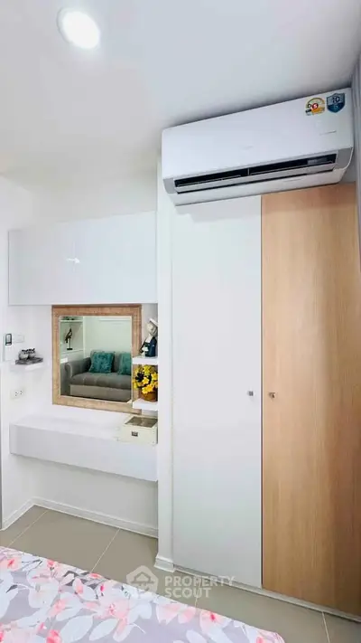 Modern bedroom with built-in wardrobe and air conditioning, featuring sleek white and wood finishes.