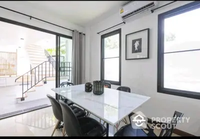 Modern dining area with sleek table and chairs, large windows, and outdoor view.