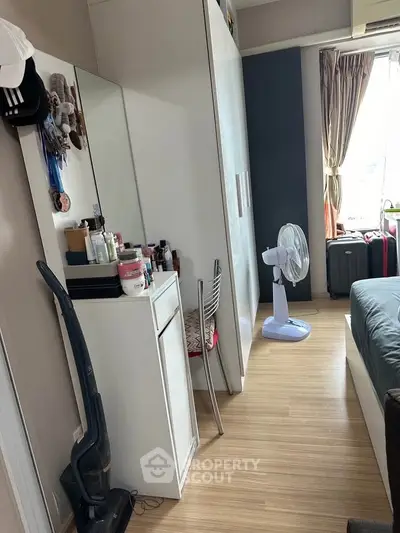 Cozy bedroom with wooden flooring, wardrobe, and natural light from large window.