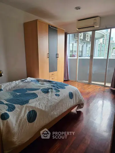 Spacious bedroom with balcony and city view, featuring wooden flooring and modern air conditioning.