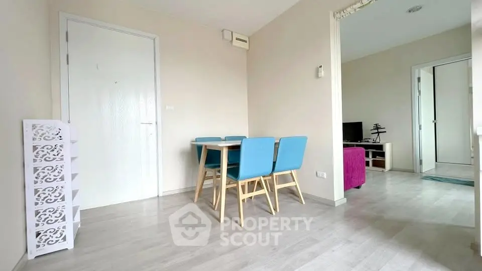 Modern apartment interior with dining area and living room, featuring stylish blue chairs and sleek flooring.