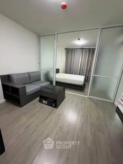 Modern studio apartment with sliding glass doors separating living and bedroom areas, featuring sleek furniture.