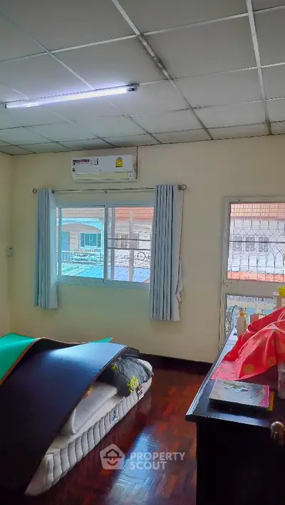Spacious bedroom with large window and air conditioning, featuring wooden flooring and natural light.