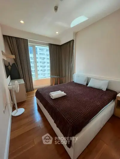 Cozy bedroom with modern decor and large window offering city views, perfect for urban living.