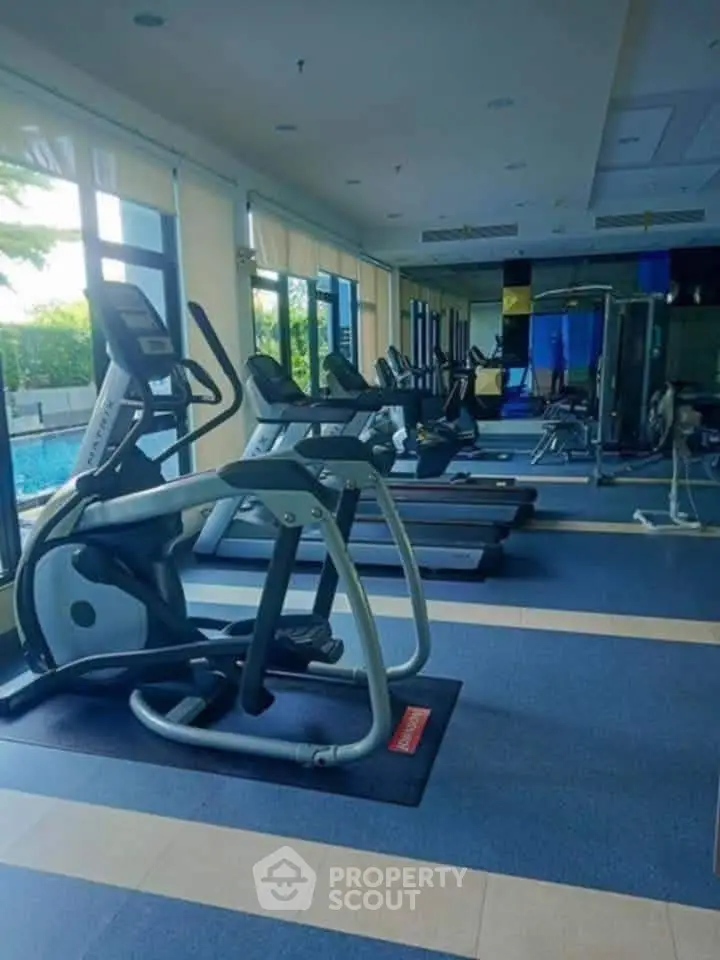Spacious gym with modern equipment and pool view in luxury apartment complex.