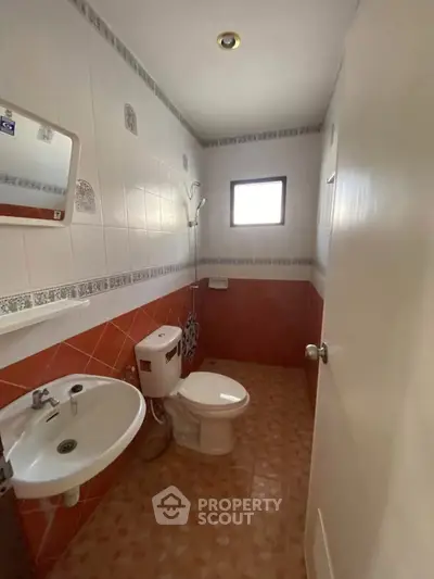Compact bathroom with tiled walls and floor, featuring a toilet, sink, and shower area.