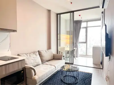 Modern living room with cozy sofa and glass partition leading to a bright study area with city view.