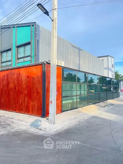 Modern industrial building with sleek glass facade and vibrant red gate, ideal for commercial use.