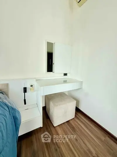 Modern bedroom with sleek white vanity and plush stool on elegant wooden flooring.
