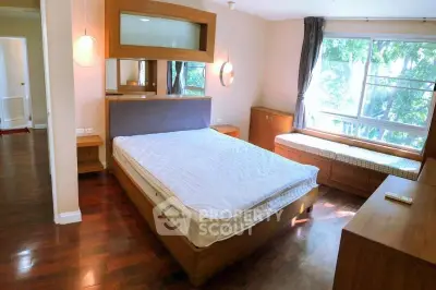 Spacious bedroom with large window and wooden furniture, offering a serene view and ample natural light.