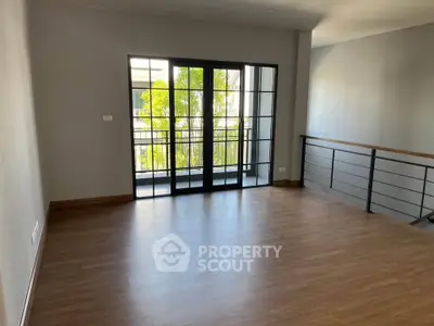 Spacious living room with large windows and balcony access, featuring elegant wooden flooring.