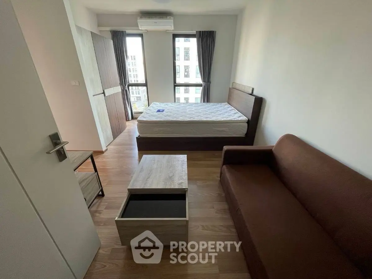 Modern bedroom with wooden flooring, cozy brown sofa, and large window view.